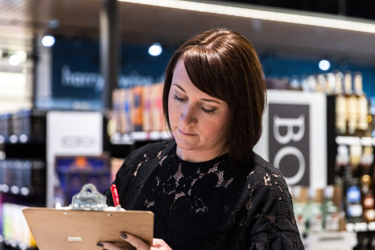 woman writing on clipboard in a liquor store