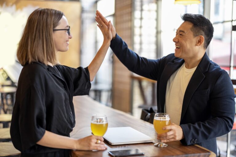 Two people high five over the bar at a brewery